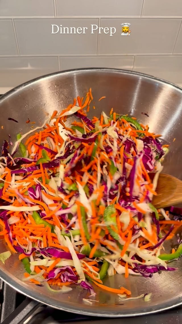 A steel wok filled with shredded red cabbage, carrots, and green beans being tossed with a wooden spoon on a stovetop, captioned Dinner Prep