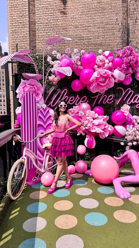 Roopsi Bansal in a pink ruffled dress with a pink bicycle at Magic Hour's Pink Bunny Beach installation, surrounded by pink balloons and flowers