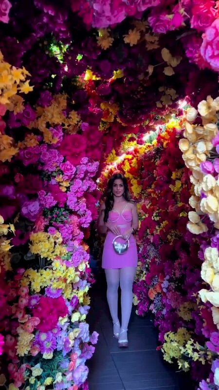 Roopsi Bansal in a pink cutout dress walking through a rooftop tunnel entirely walled and ceilinged in flowers