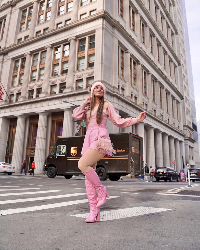Roopsi Bansal in an all-pink outfit with a feather-trim bag and pink boots, twirling in a Financial District intersection