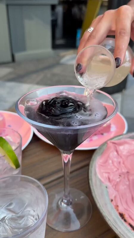 A dark cocktail being poured tableside at Magic Hour Rooftop & Lounge's Pink Pumpkin Patch Halloween pop-up in NYC