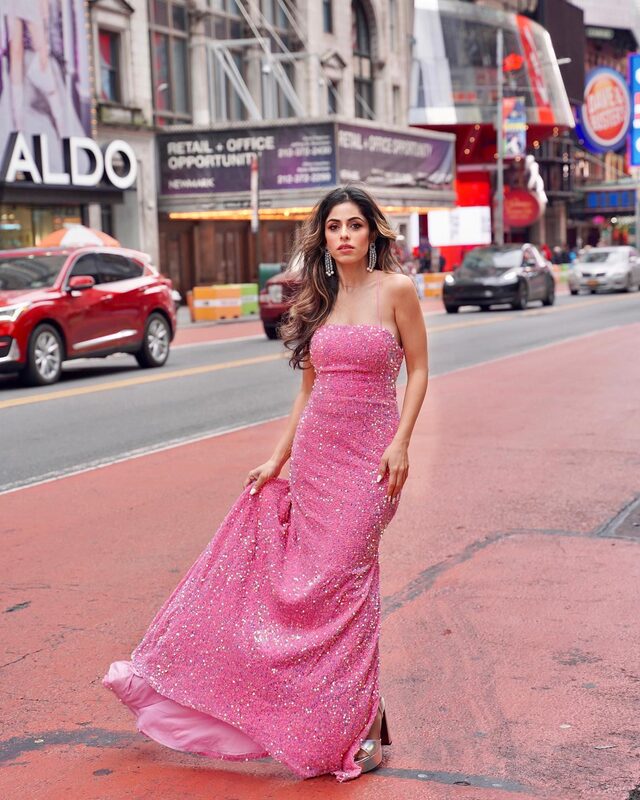Roopsi Bansal in a pink sequin gown standing in the middle of a Times Square street with traffic and billboards behind her