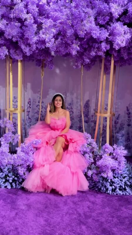 Roopsi Bansal in a huge pink tulle gown sitting on a swing surrounded by a purple wisteria-style floral installation