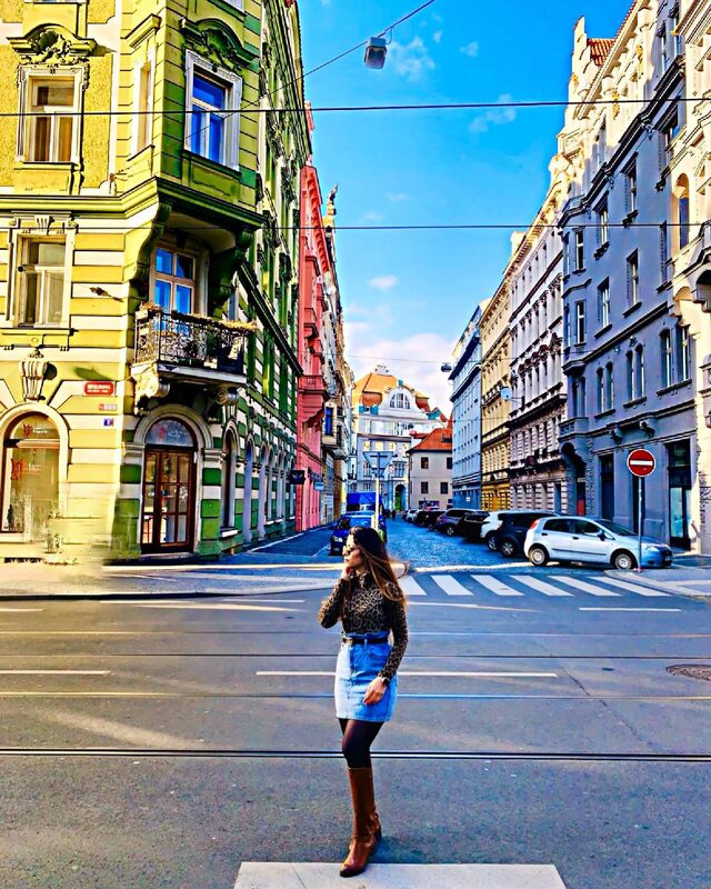 Standing in the middle of a colorful Prague street intersection wearing a leopard-print top, denim skirt, black beret, and cognac boots