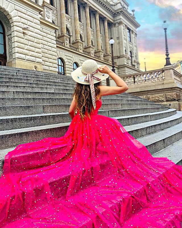 Roopsi Bansal in a hot-pink sequined gown and straw hat on the steps of a grand neoclassical building in Prague