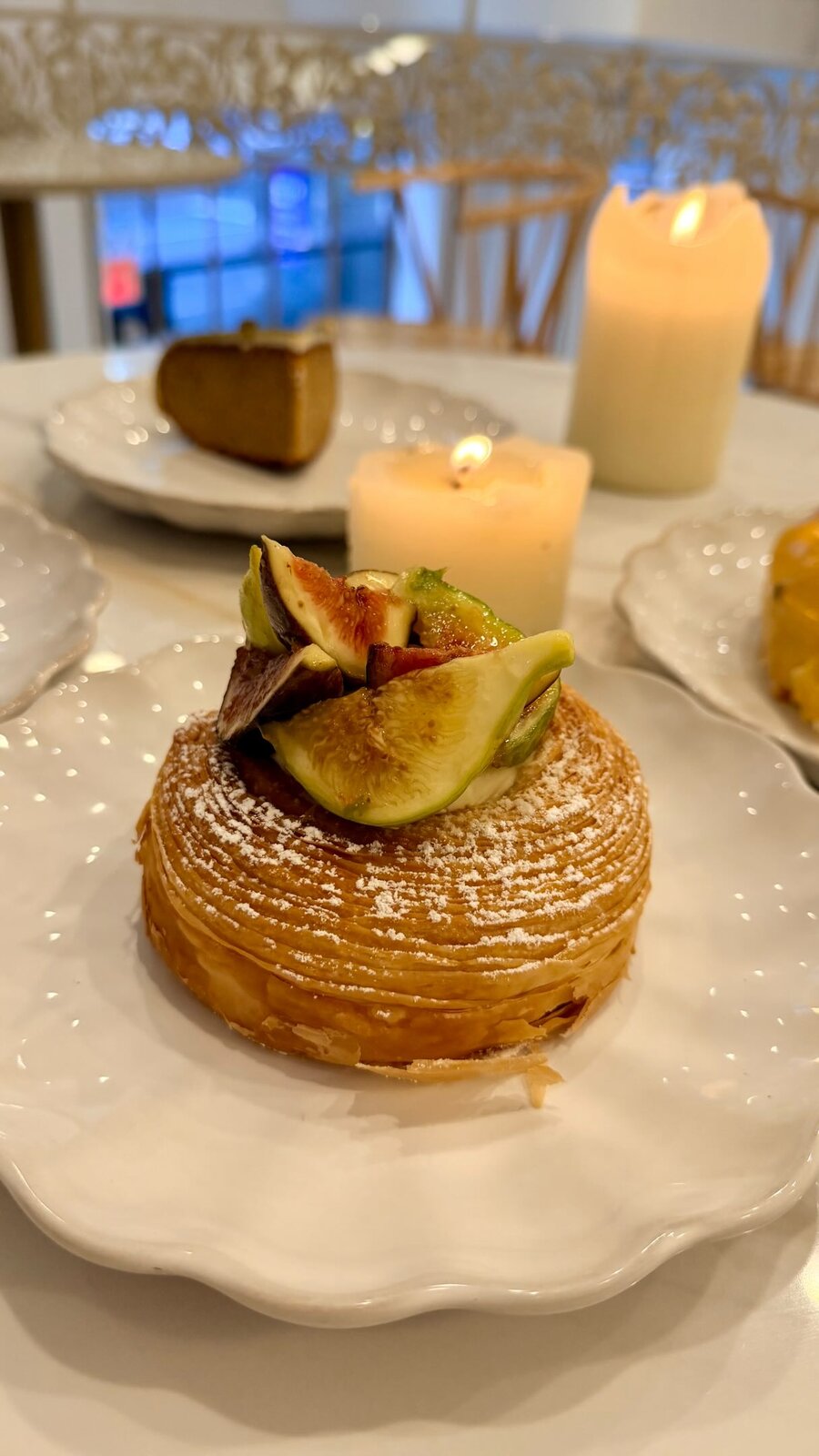 A pastry topped with fresh figs and powdered sugar on a white plate at a candlelit café table