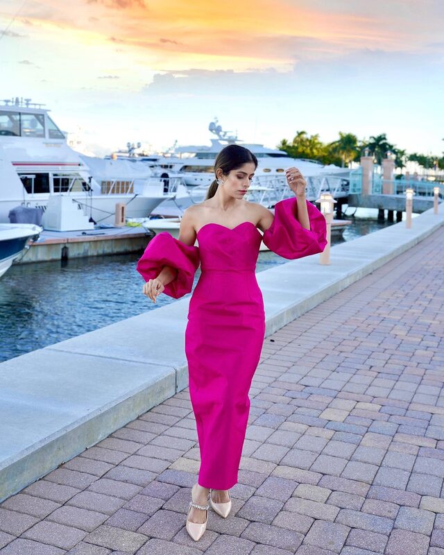 Roopsi Bansal in a fuchsia off-shoulder maxi dress with dramatic puff sleeves, walking along a marina lined with yachts at sunset