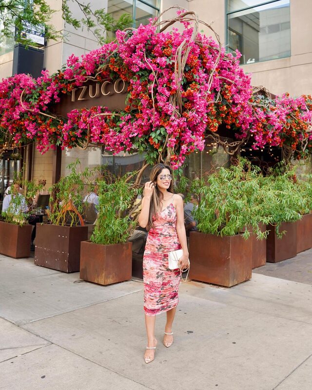 Roopsi Bansal in a pink floral mesh bodysuit and midi skirt, standing beneath the bougainvillea-draped storefront of Tzuco restaurant in Chicago