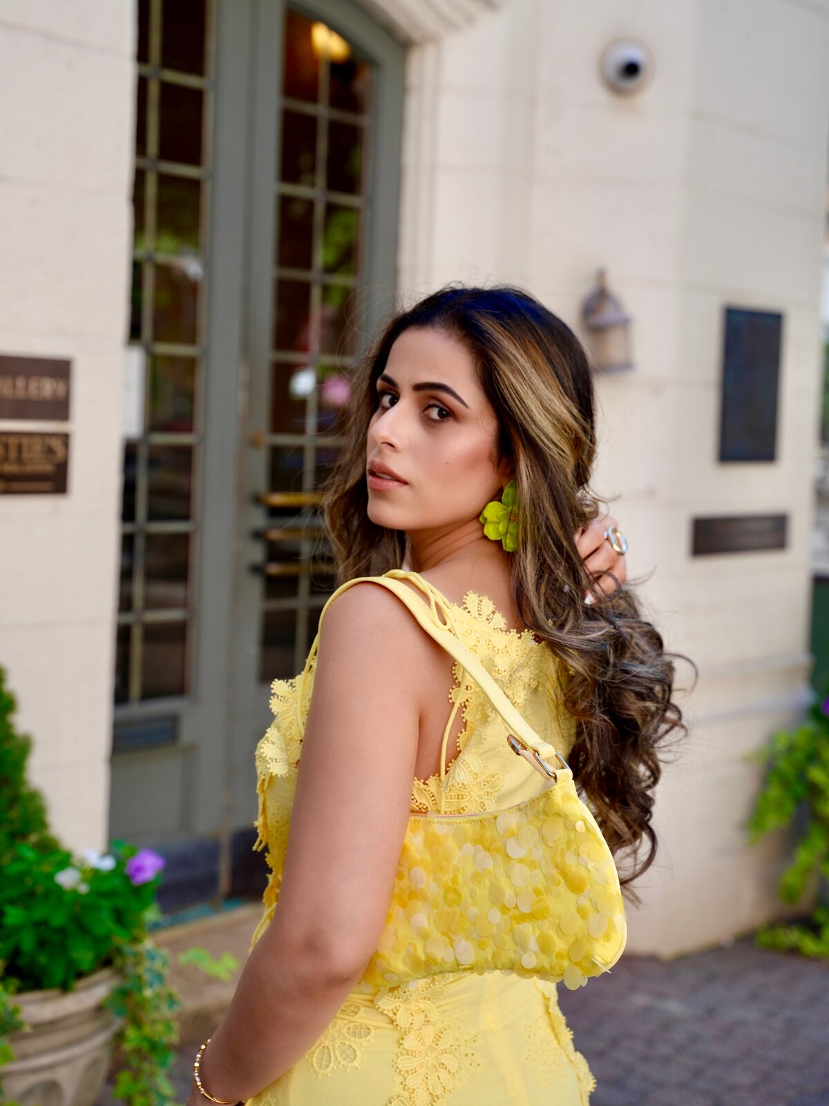 Roopsi Bansal glancing back over her shoulder in a yellow lace dress in front of a gallery entrance
