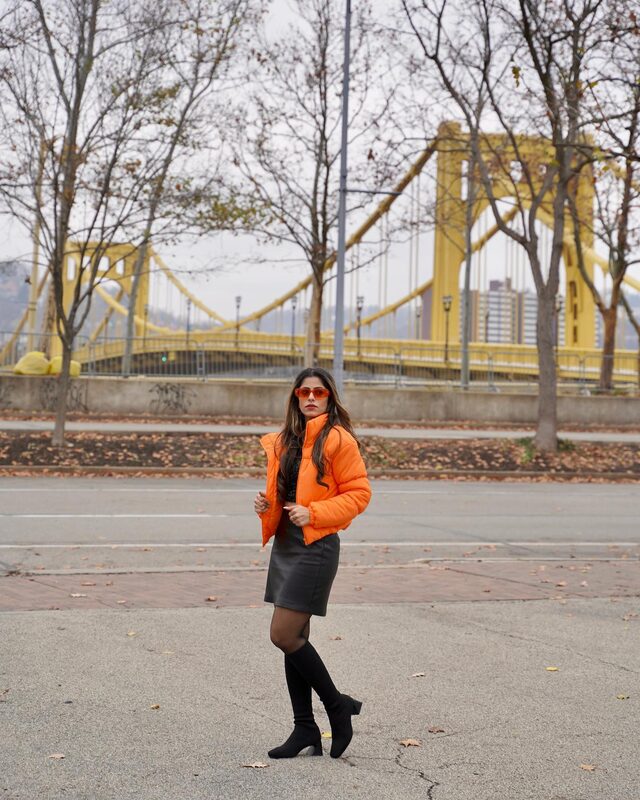 Roopsi Bansal in a puffer jacket standing on the Roberto Clemente Bridge in Pittsburgh