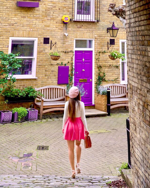 Roopsi Bansal from behind in a hot pink skater skirt and pearl-trim beret, walking toward a violet front door in the Warwick Square mews, London