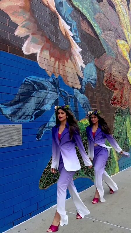 Roopsi Bansal in a purple ombré blazer set and floral crown walking past a colorful mural in Philadelphia