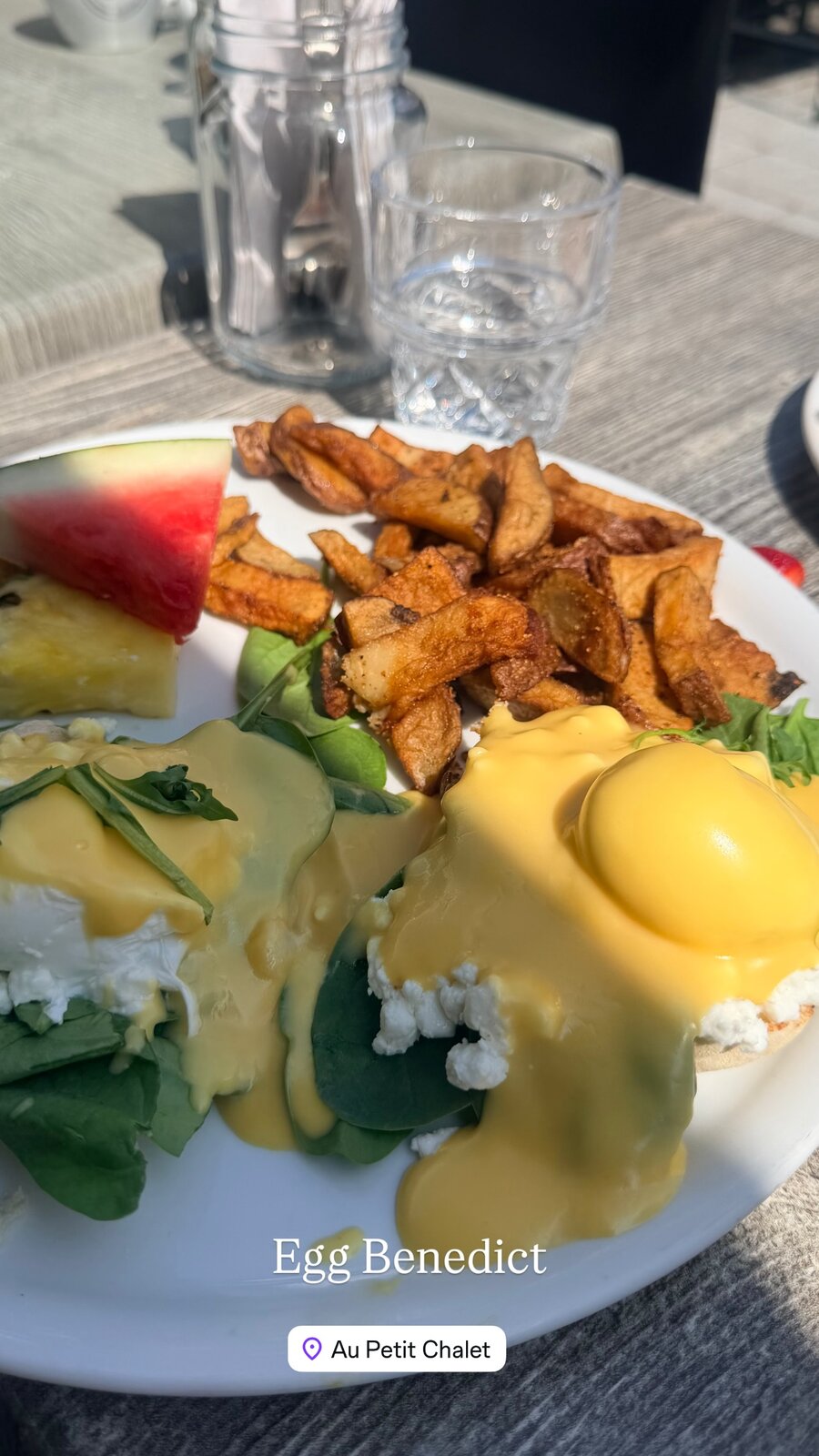 A plate of Egg Benedict with hollandaise sauce, home fries, and watermelon at Au Petit Chalet in Quebec City