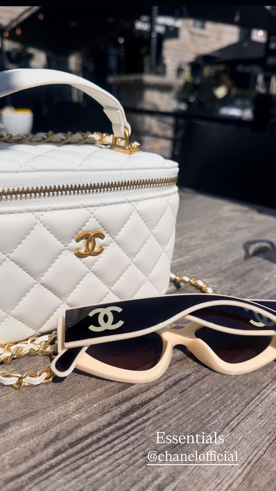 A quilted white Chanel vanity case and cream Chanel sunglasses on a wooden patio table, captioned Essentials