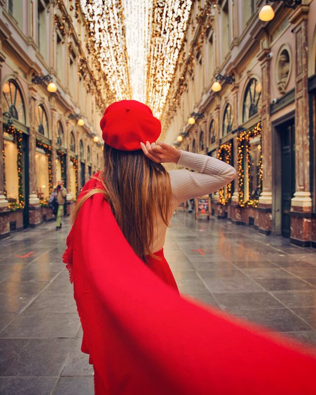 Roopsi Bansal from behind in a red beret and long red scarf, standing in the golden-lit Galeries Royales Saint-Hubert shopping arcade in Brussels
