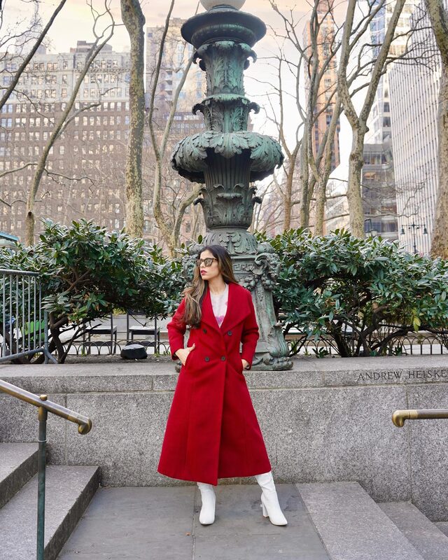 Roopsi Bansal in a wide lapel double-breasted red longline coat standing in front of the ornate fountain in Bryant Park