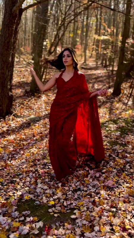 Roopsi Bansal in a red sequined saree walking through a forest floor covered in fallen autumn leaves