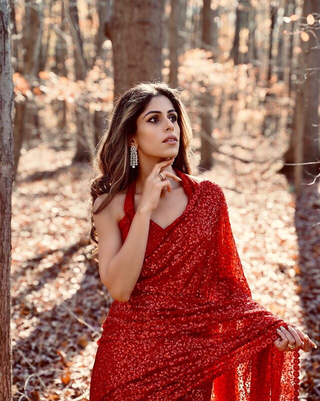 Roopsi Bansal in a red sequin saree and statement earrings standing among bare winter trees on Christmas Day