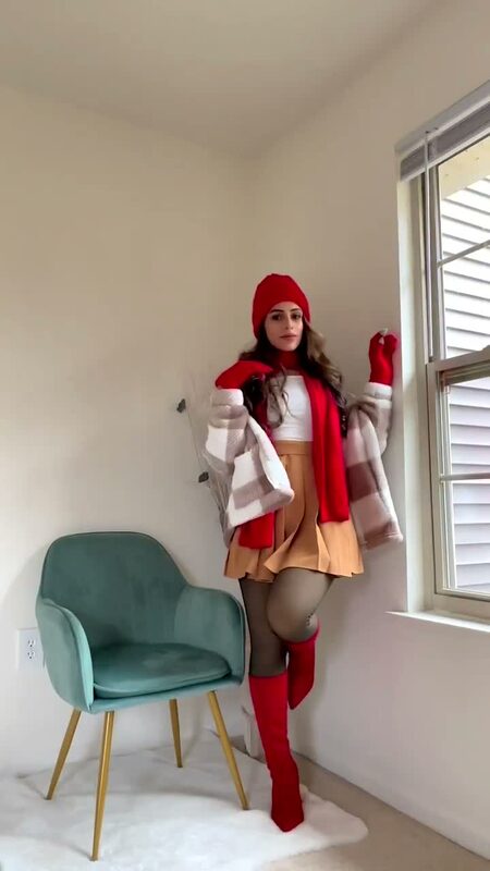 Roopsi Bansal in a red beanie, scarf, gloves, teddy coat, and red boots posing at home by a window