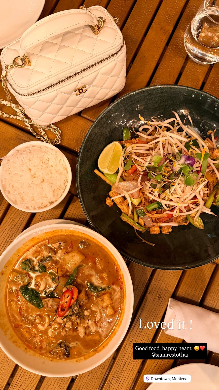 A Thai dinner spread of green curry, noodles with bean sprouts, and rice, next to a white quilted handbag on a wooden table