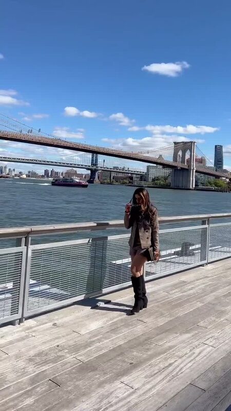Roopsi Bansal in a blazer and shorts set on the Seaport pier under clear blue skies, Brooklyn Bridge behind her