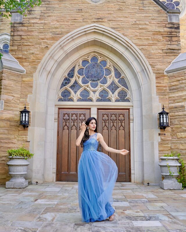 Roopsi Bansal in a blue sequin-bodice tulle gown from EverPretty, twirling in front of a Gothic stone church doorway with a stained glass window in Atlanta