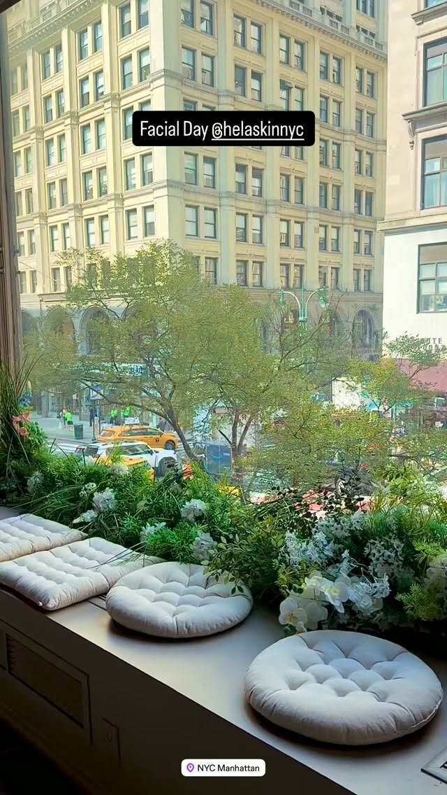 A sunlit window seat with cushions and greenery overlooking a Manhattan street