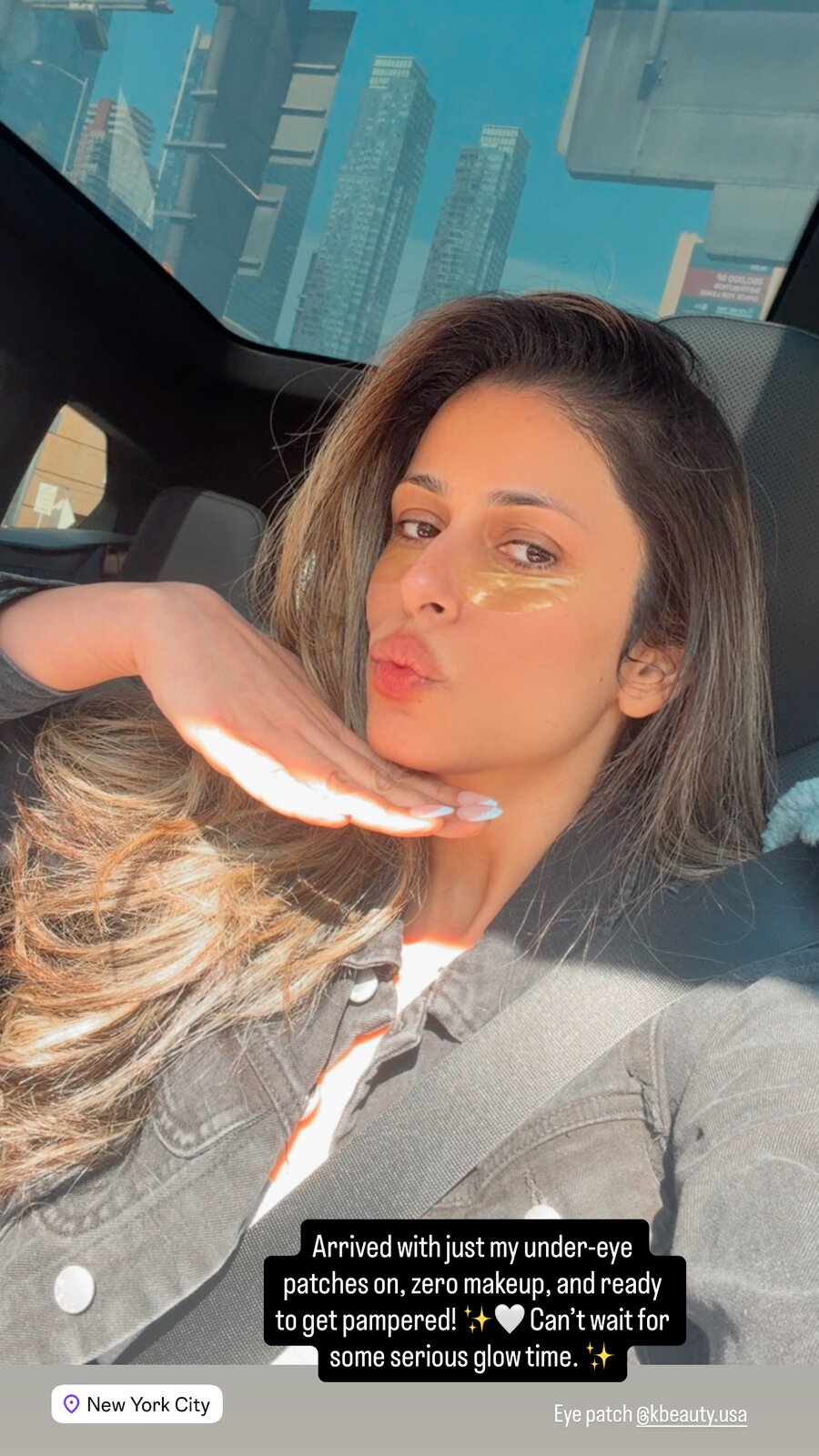 Roopsi Bansal taking a car selfie wearing gold under-eye patches, NYC skyline through the sunroof
