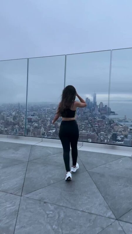 Roopsi Bansal in workout clothes on the glass-walled observation deck at Edge NYC overlooking the Manhattan skyline