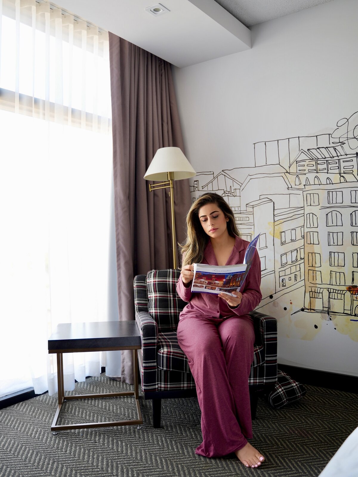 Roopsi Bansal reading a city guide magazine in a mauve pajama set in a plaid armchair