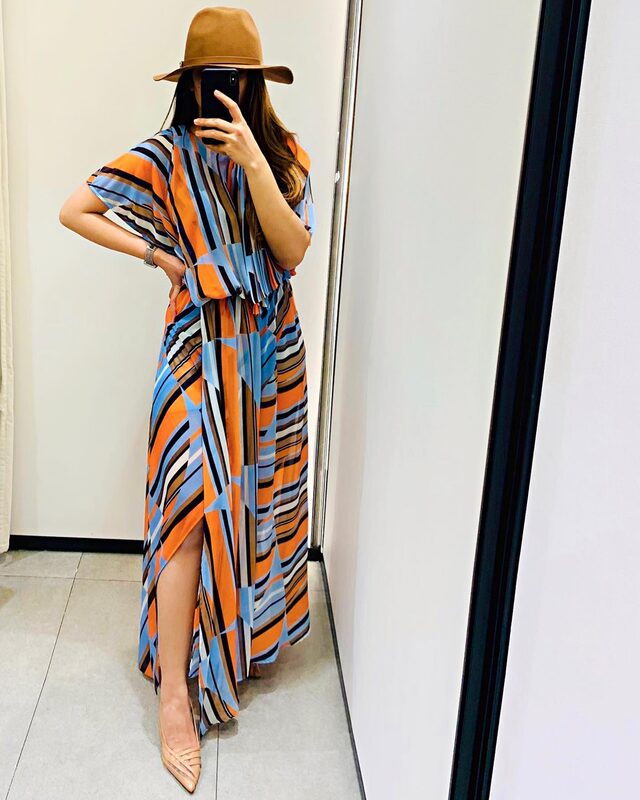 Mirror selfie in a geometric orange, blue, and black striped maxi dress and a wide-brim tan hat, in a fitting room