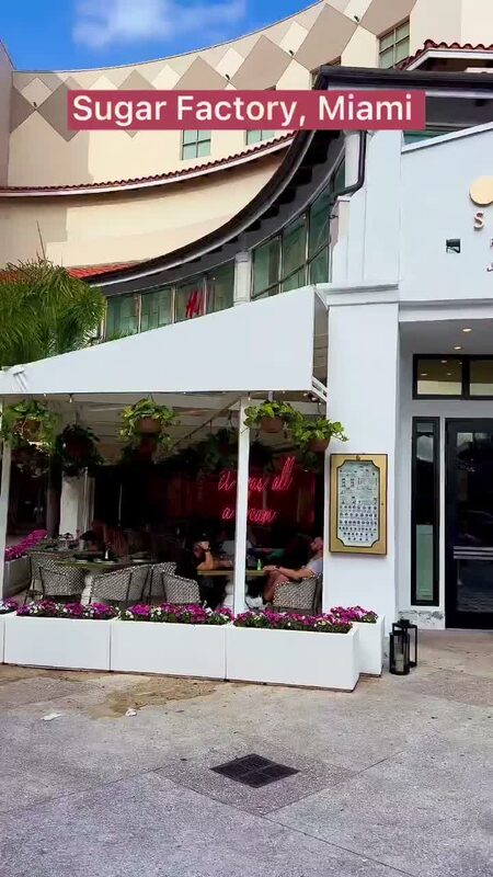 The colorful storefront of Sugar Factory in Miami, with hanging plants and a neon sign reading 'it was all a dream' visible through the window