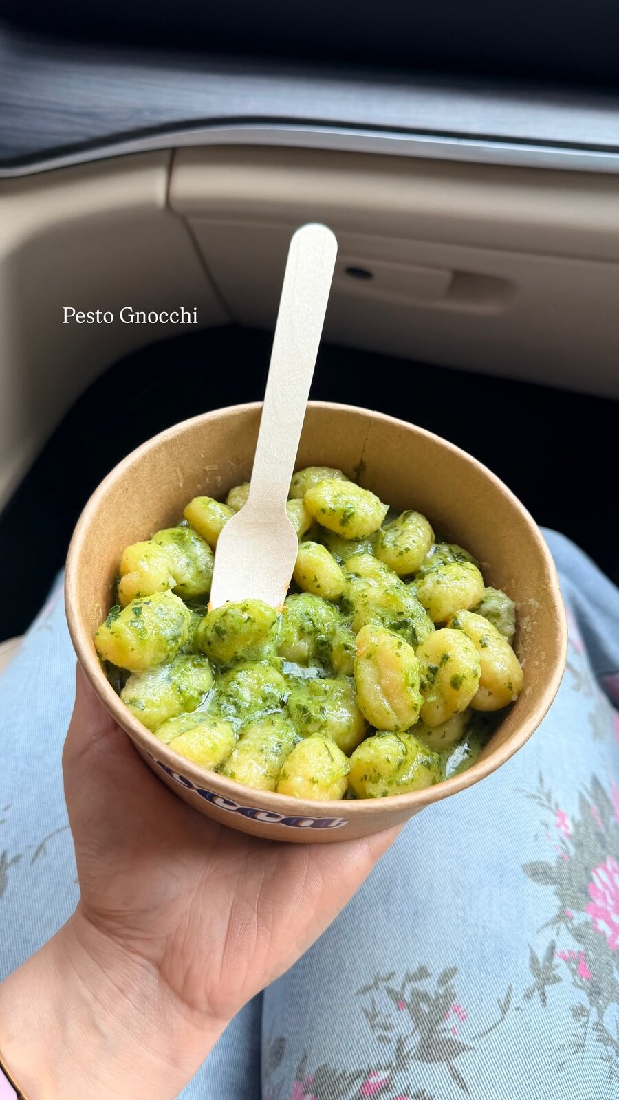 A takeout container of pesto gnocchi held on a lap in the car