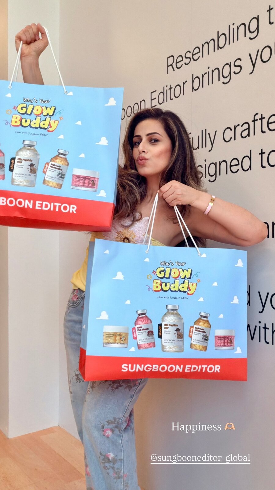 Roopsi Bansal holding up two Sungboon Editor 'Who's Your Glow Buddy' gift bags filled with skincare ampoules and jars, at a Toy Story-themed popup