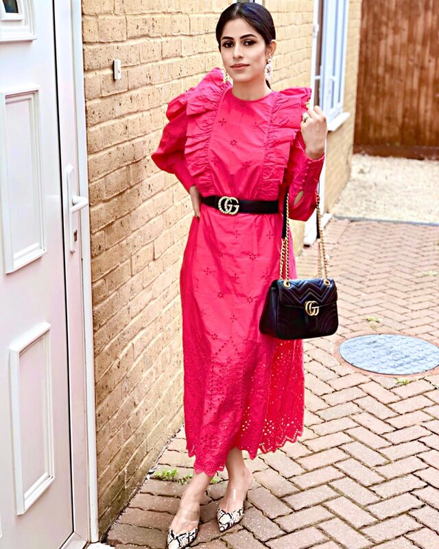 Standing by a brick doorway wearing a hot pink eyelet-embroidered midi dress with a black Gucci belt, Gucci Marmont bag, and snakeskin heels