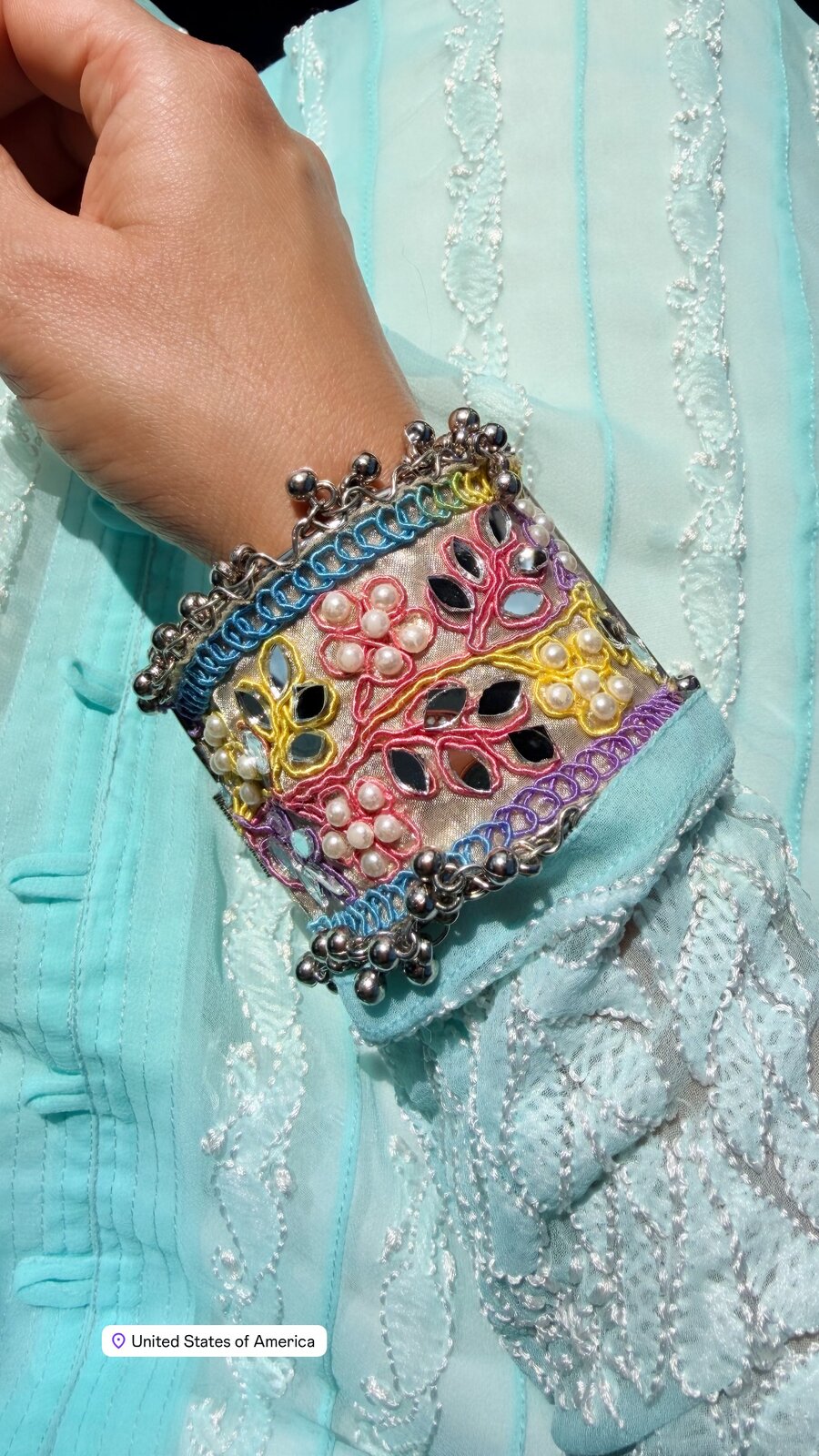 Close-up of a mirror-work and pearl cuff bracelet worn over a pastel blue embroidered sleeve
