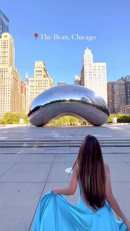 Roopsi Bansal from behind in a cloud blue flowing gown, facing Cloud Gate, the mirrored bean sculpture, at Millennium Park in Chicago