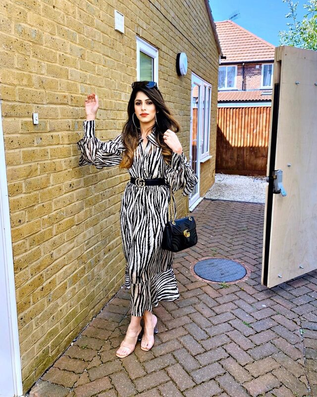 Standing at a brick doorway wearing a zebra-print maxi dress with a Gucci belt and Gucci Marmont bag, hoop earrings, and clear strap heels
