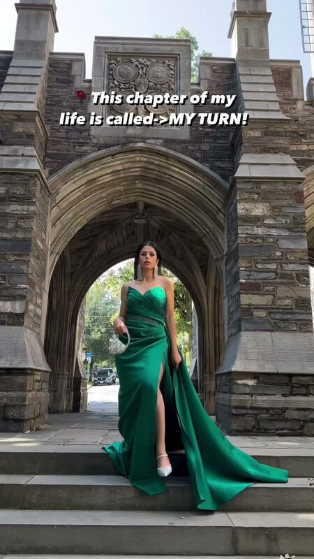 Roopsi Bansal in an emerald green satin gown with a thigh slit standing in a Gothic stone archway at Princeton University