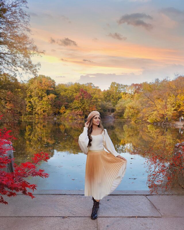Roopsi Bansal in a cream cardigan and tan pleated skirt by the Central Park lake at sunset