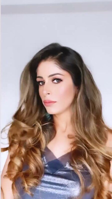 Roopsi Bansal with soft waves, winged eyeliner and a nude-pink lip, wearing a shimmery top