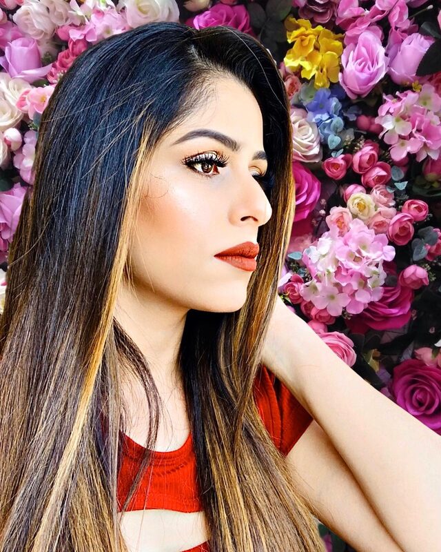 A profile portrait against a wall covered in pink, yellow, and purple flowers, wearing a red top and a bold matte red lip