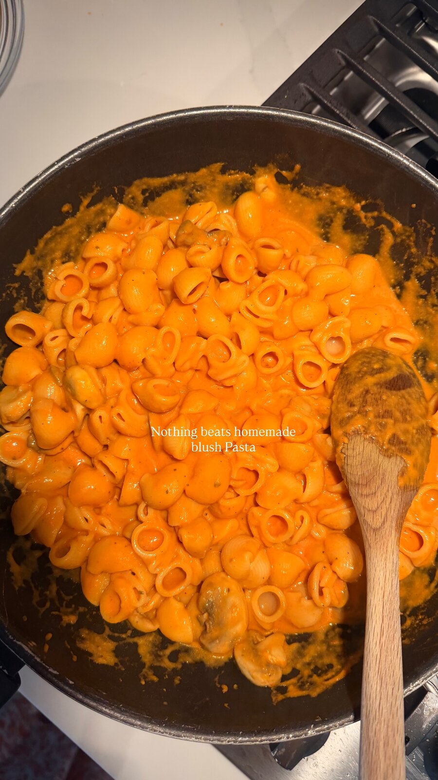 Shell pasta coated in a creamy orange blush sauce in a skillet with a wooden spoon