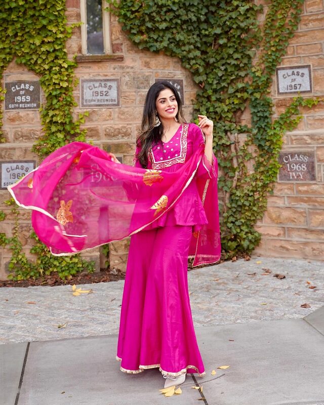 Roopsi Bansal twirling in a magenta sharara set from The Loom in front of an ivy-covered stone wall