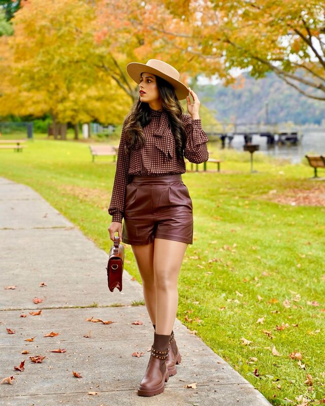 Roopsi Bansal in a printed blouse and brown faux-leather shorts from Express by a riverside park path