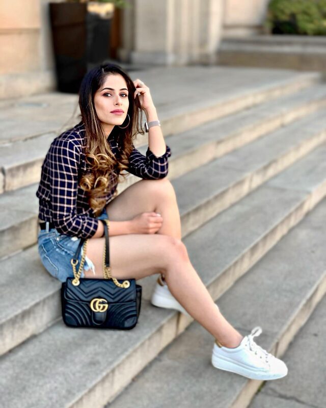 Roopsi Bansal sitting on stone steps in a navy plaid shirt and denim shorts in Prague, Czech Republic