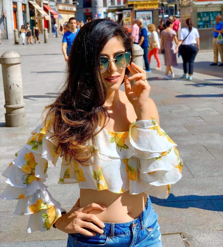 Standing in a sunny Madrid plaza wearing a lemon-print off-shoulder crop top and ripped jeans, round sunglasses pushed up, hand on hip