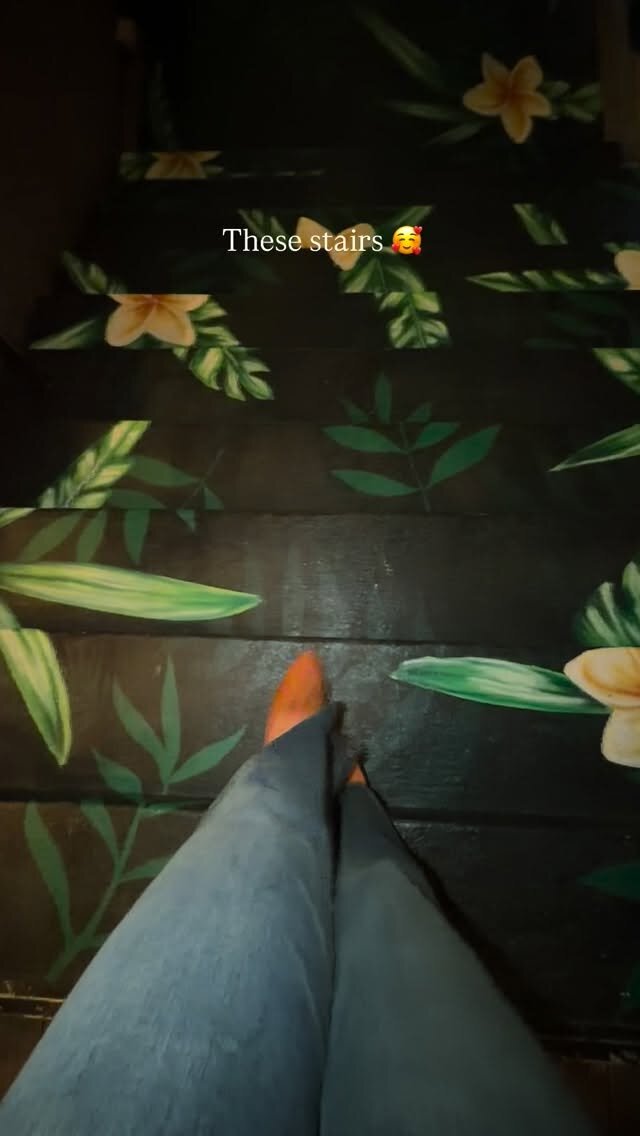 A hand-painted staircase covered in green leaves and flowers, with a foot stepping down, captioned These stairs