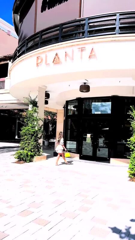 Roopsi Bansal walking toward the entrance of Planta restaurant in West Palm Beach, Florida, carrying a yellow bag