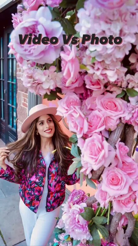 Roopsi Bansal in a pink floral-print puffer jacket and hat beside a wall of oversized faux roses and peonies